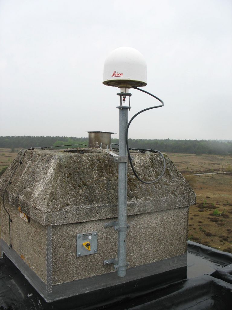 The GNSS antenna is mounted on a short mast on: the roof of Radio Kootwijk, nearby, and in sight of, the former Kootwijk Observatory for Satellite Geodesy (KOSG).
