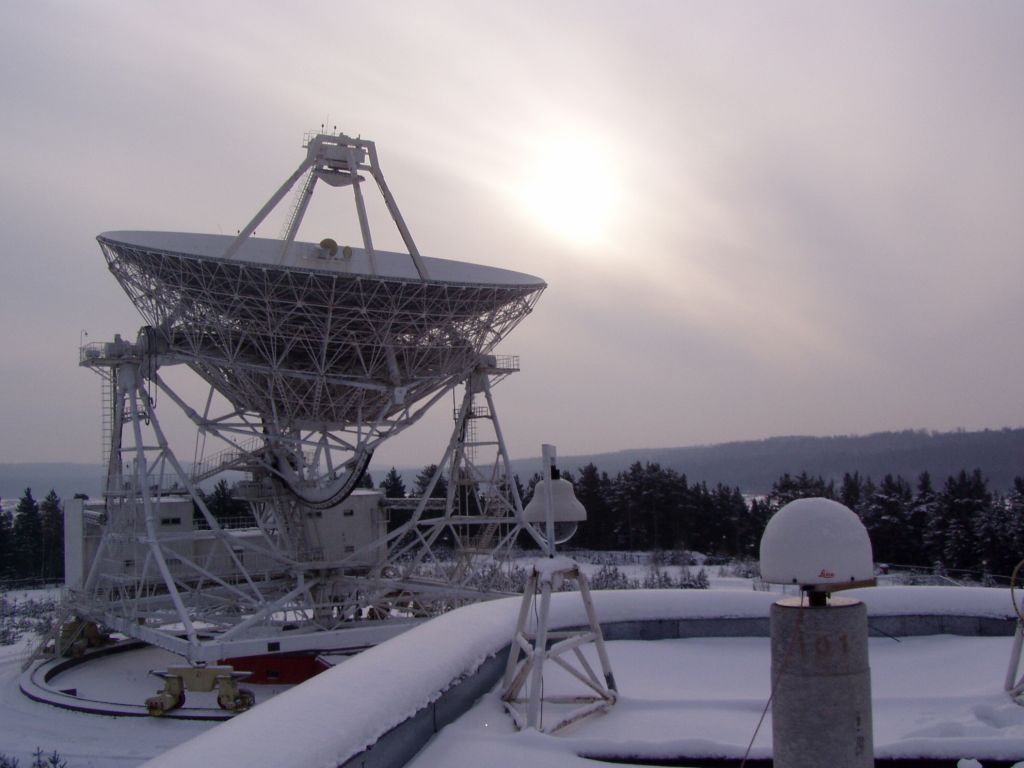 Leica AT504 antenna with radome on the concrete pillar on the roof of 2-store laboratory building at the Svetloe Radio Astronomy Observatory (SvRAO) in about 100 km from St. Petersburg, Russia. The receiver is installed on Dec 1, 2004. On the left - 32-m VLBI radio telescope RTF-32, IVS station SVETLOE, participating in the IVS observing programs till Mar 2003.