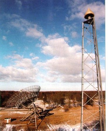 permanent EUREF GPS station at the Westerbork Synthesis Radio Telescope (WSRT), The Netherlands. The station is co-located with an SLR laser platform (no observations yet available) and has facilities for absolute gravimeters. The height of the antenna is stabilized by means of an invar-wire running down to the bottom. In the background one of the fourteen 25-meter dishes of the synthesis radio telescope is visible.