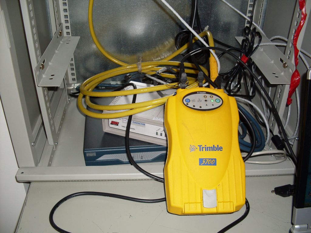 The old GNSS receiver Trimble 5700 allocated in RAC cabinet with belonging communication router, LAN cables and charging adapter.