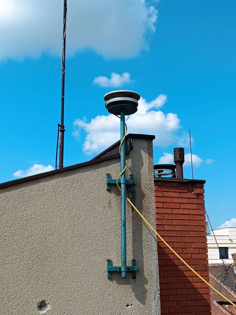 The iron pillar with mounted CORS antenna TRM41249.00 is attached to the concrete wall on the local cadaster building roof with belonging antenna cable.