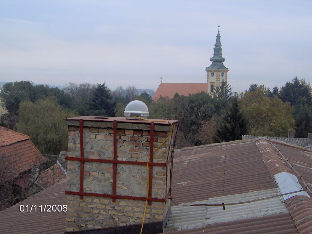 The preview of Trimble Zephyr Geodetic antenna with protective radome installed on the metal mounting base fixed to iron reinforcement console which is attached to the brick chimney on the roof of local cadaster building. 